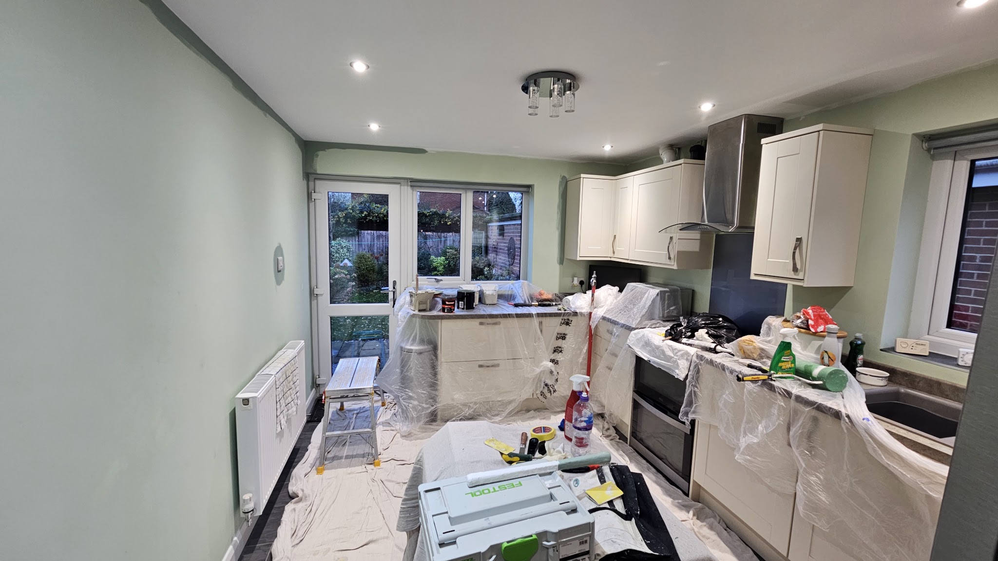 Kitchen with sage green walls mid-job, floor protected with dust sheets